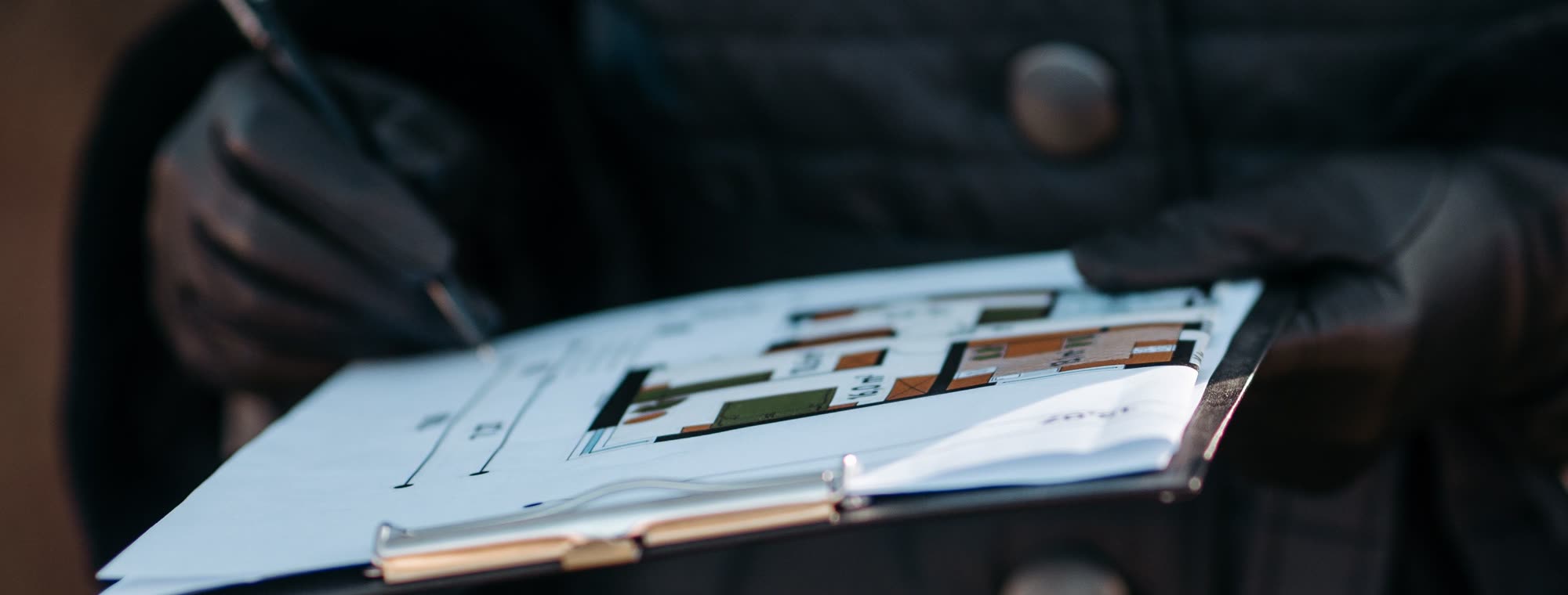 A person in gloves holding a clipboard with a printed floor plan, pen in hand