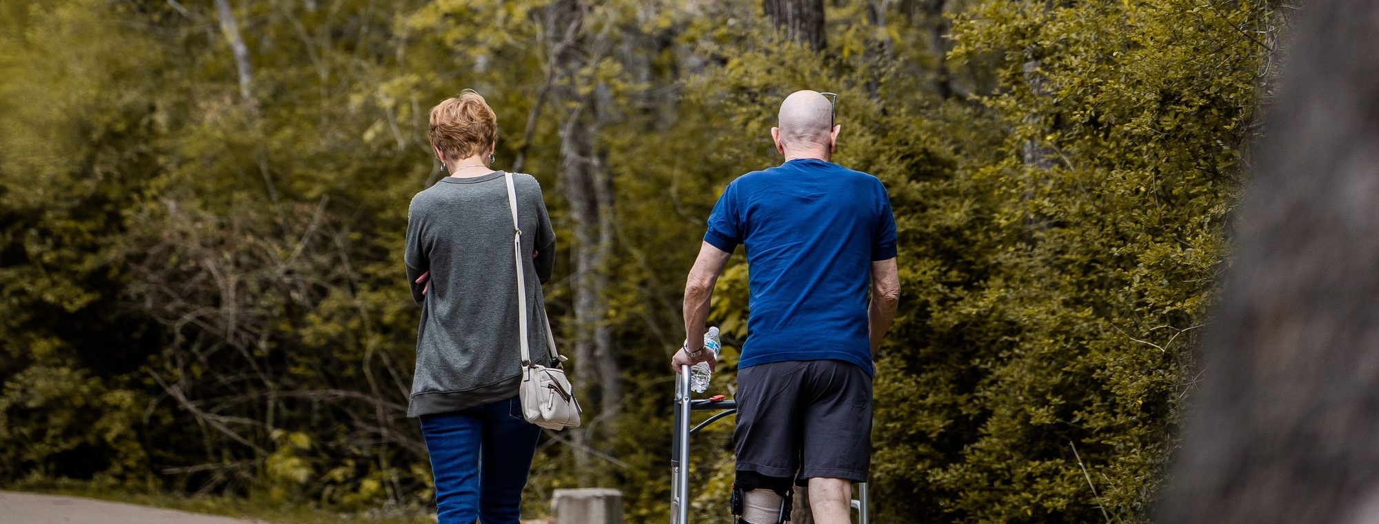A couple walking outdoors, one using a walking frame during recovery