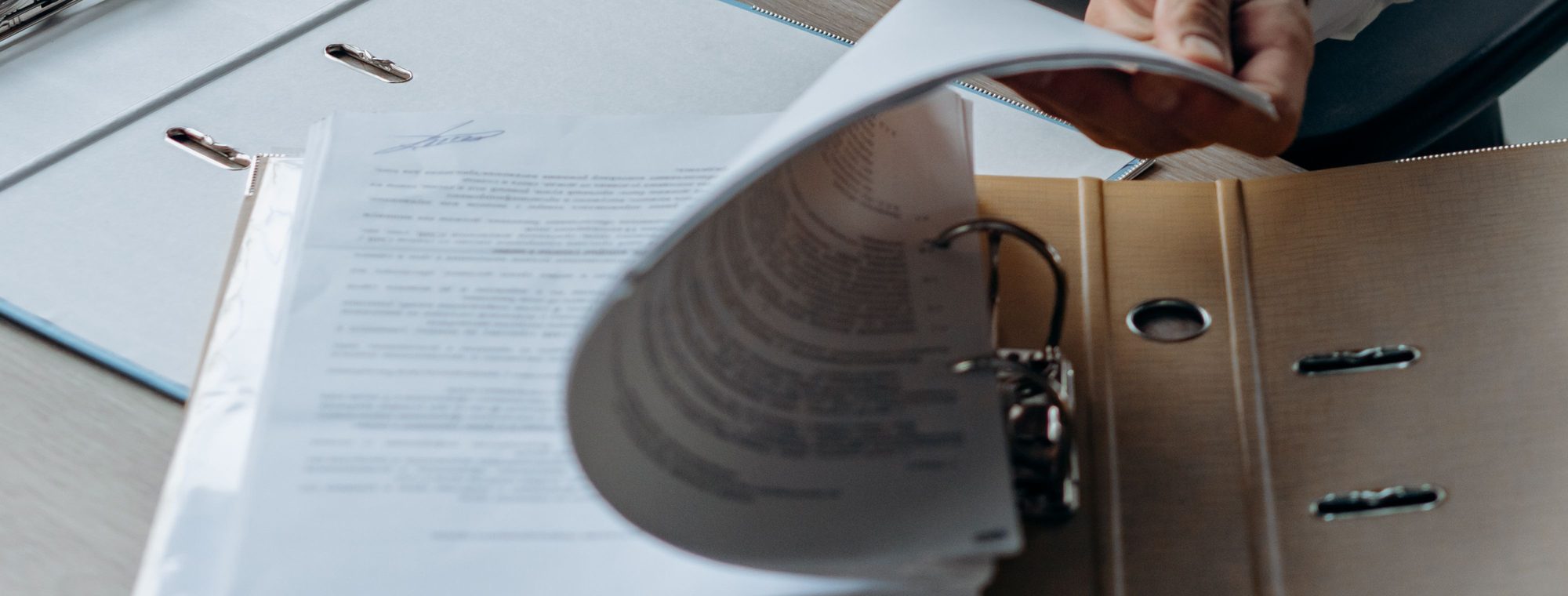 A hand reviewing paperwork in a lever-arch file at a desk