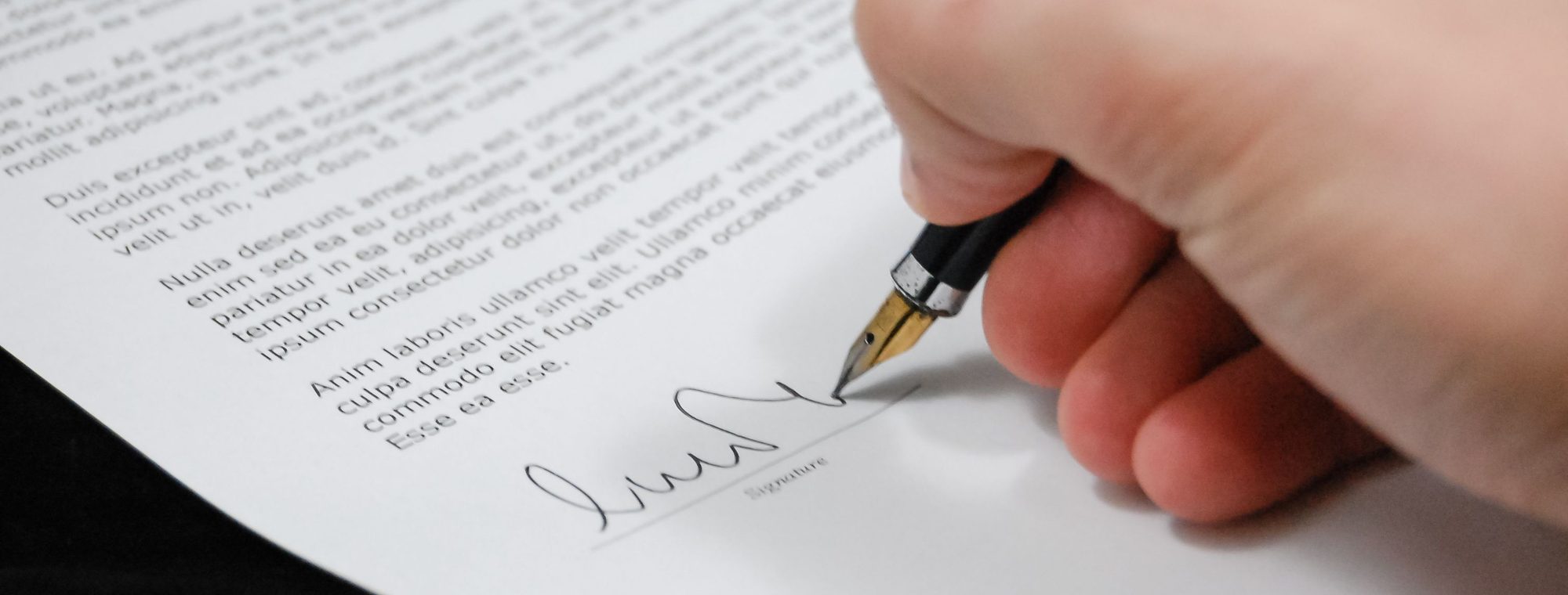 A hand signing a legal document with a fountain pen