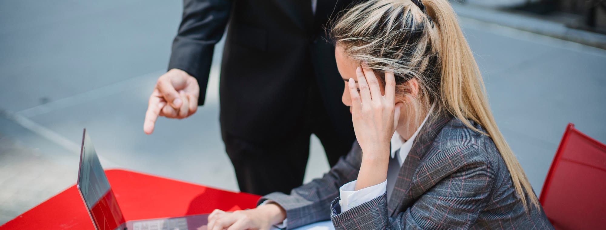 A workplace confrontation at an outdoor table, one person pointing while the other reacts